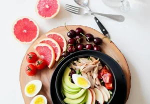 A vibrant breakfast flat lay featuring a mix of fruits, avocado, eggs, tomatoes, and sliced meats on a wooden platter.