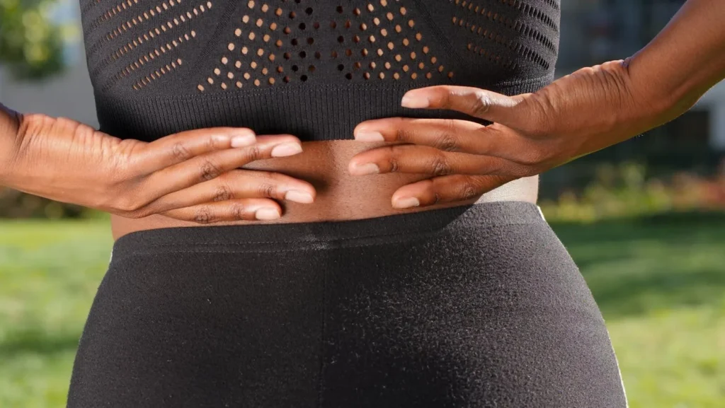 Close-up of a woman's hands gripping her painful back while outdoors.