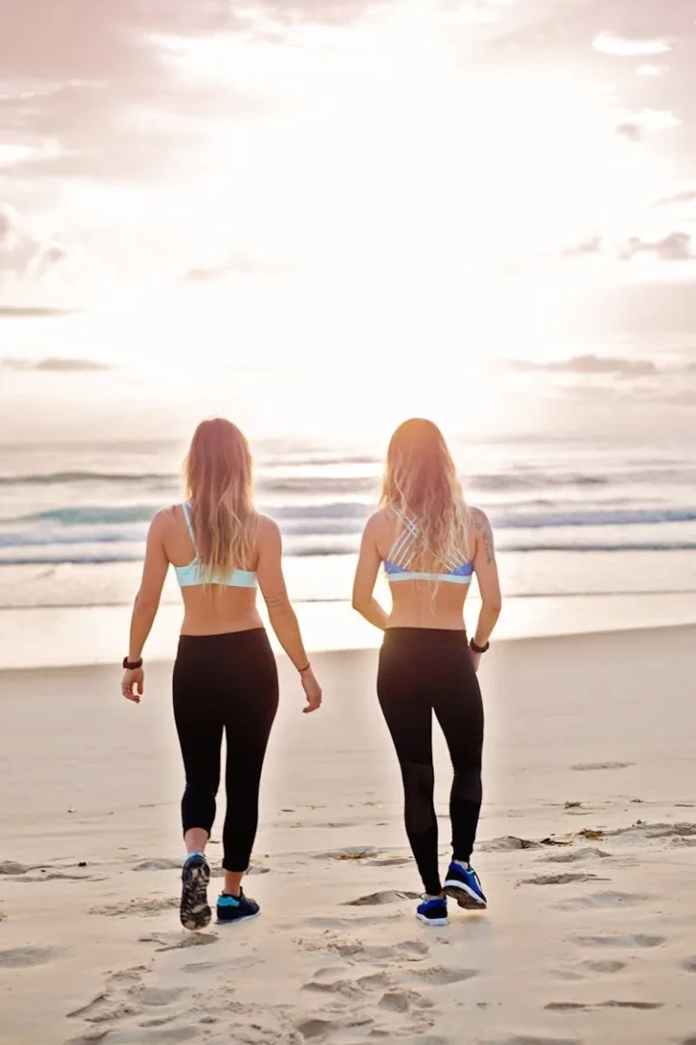 Two women walk along a sandy beach at sunset, enjoying a peaceful evening stroll by the ocean.