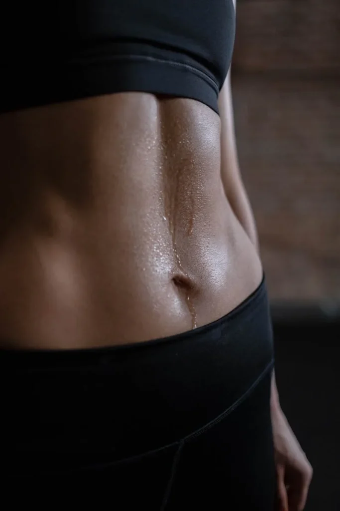 A close-up of a fit woman's toned abdomen with sweat, emphasizing fitness and strength.