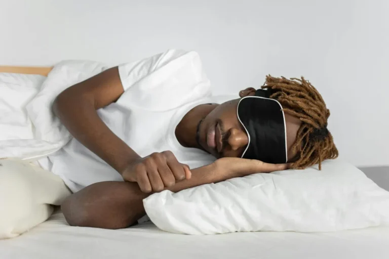 A relaxed African American man sleeping in bed wearing a black sleep mask, promoting restful sleep.