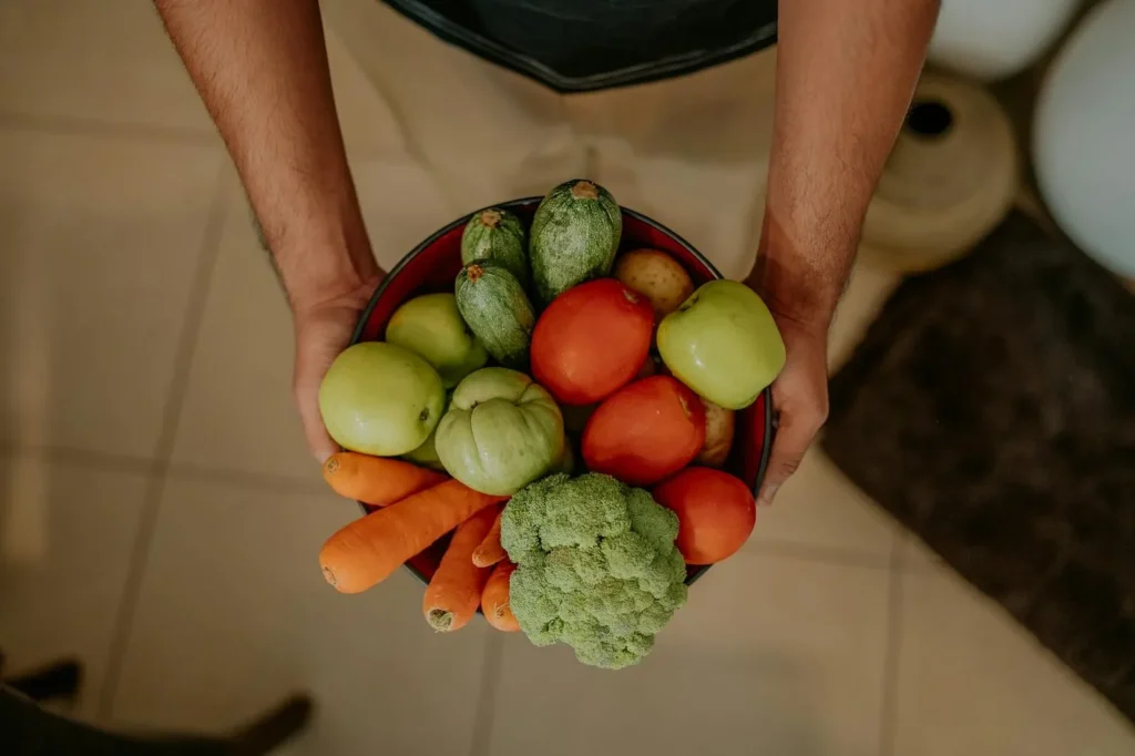 A variety of colorful fresh vegetables held in a bowl by a man's hands, showcasing healthy eating.