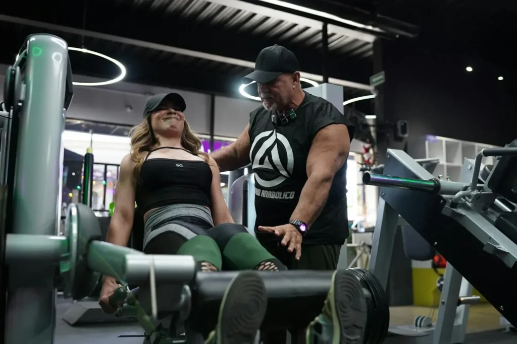 A personal trainer assists a woman with a leg press exercise in a modern gym setting.